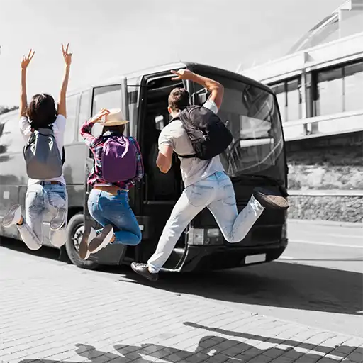 Junge Leute springen, mit Rücksäcken, vor einem Reisebus auf und ab.